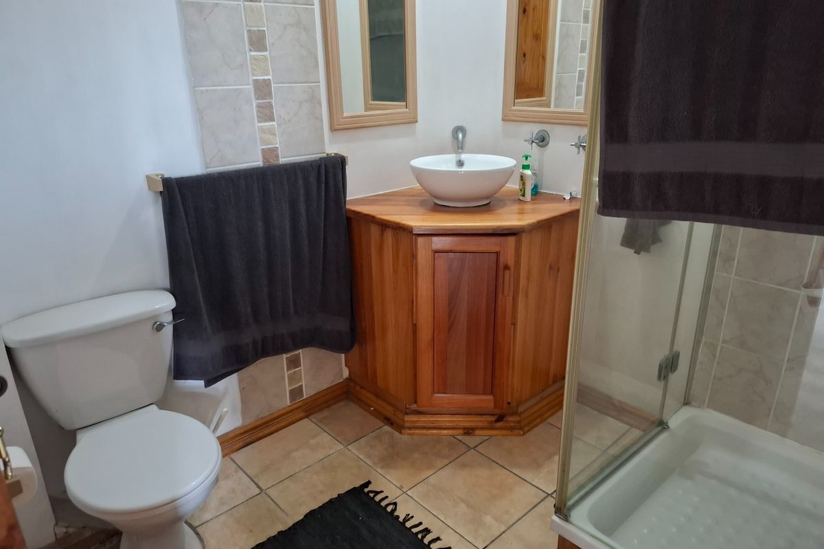 A functional bathroom featuring a corner timber vanity with a vessel sink, a standard toilet, and a glass-enclosed shower with tiled finishes.