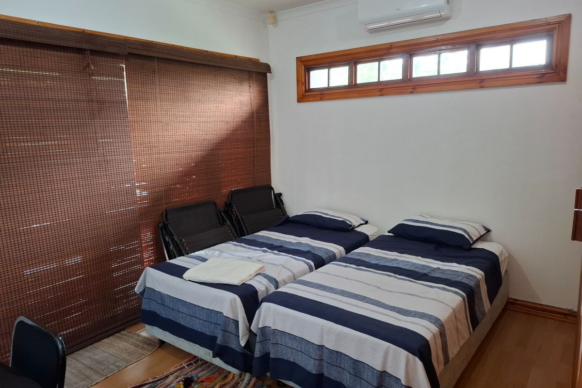 A functional bedroom featuring laminate flooring, a wall-mounted split-system air conditioner, and timber-framed windows with integrated blinds.