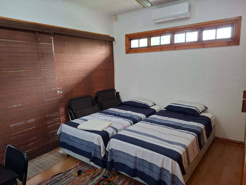 A functional bedroom featuring laminate flooring, a wall-mounted split-system air conditioner, and timber-framed windows with integrated blinds.