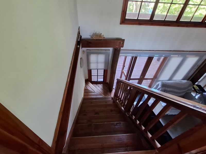 A view looking down a timber staircase featuring a wooden balustrade, natural wood finishes, and large windows allowing for ample natural light.