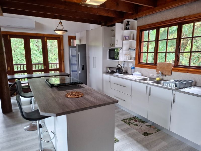 Modern kitchen featuring a central island with integrated hob, white cabinetry, timber ceiling beams, and direct access to an outdoor deck area.