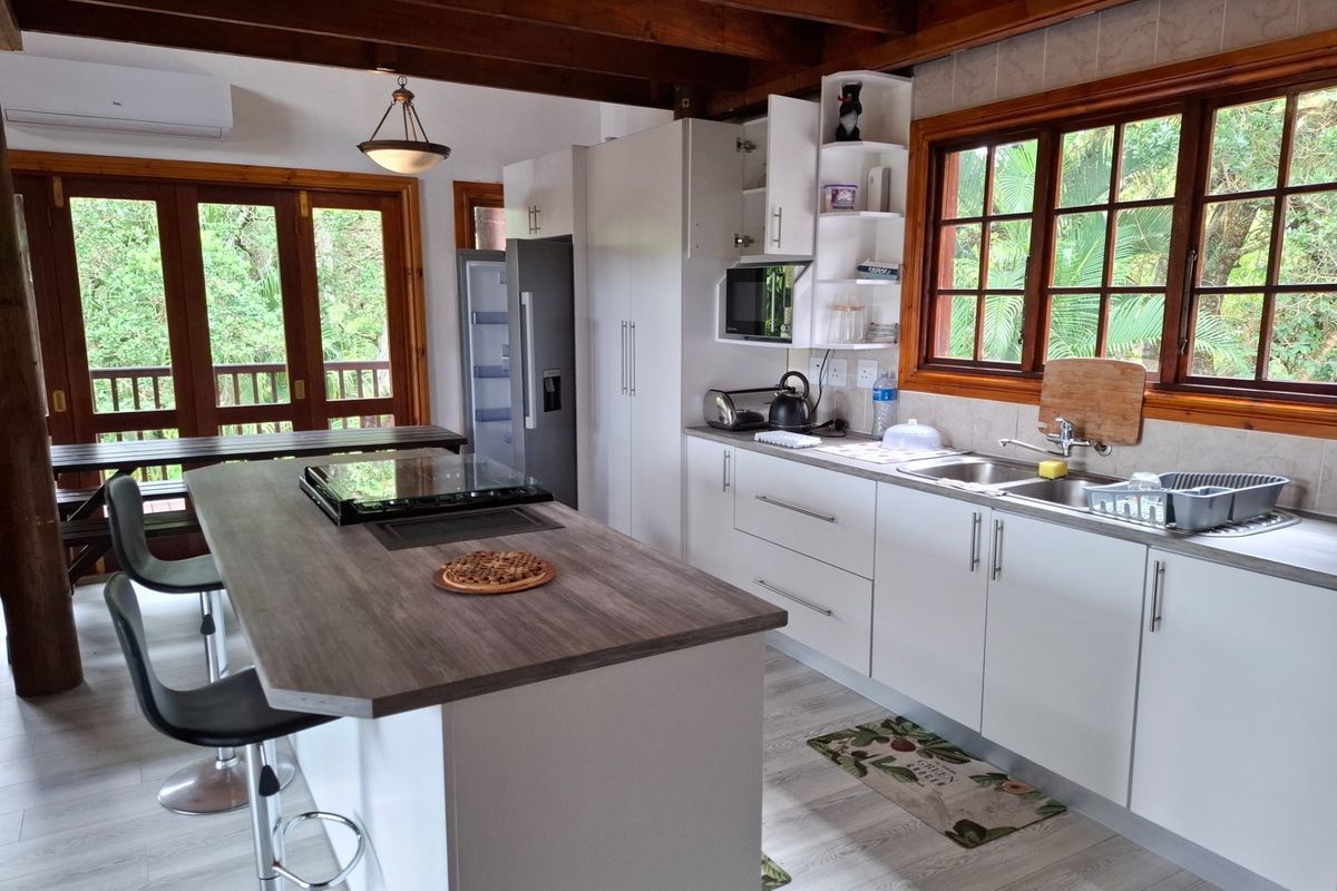 Modern kitchen featuring a central island with integrated hob, white cabinetry, timber ceiling beams, and direct access to an outdoor deck area.