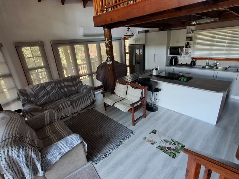 Open-plan living area featuring a modern kitchen with island, exposed timber beams, and a mezzanine level, creating a spacious and functional layout.