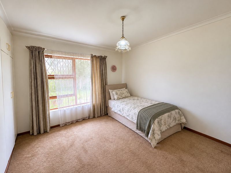 A well-maintained bedroom featuring neutral carpeting, built-in storage cupboards, and a window fitted with security bars.