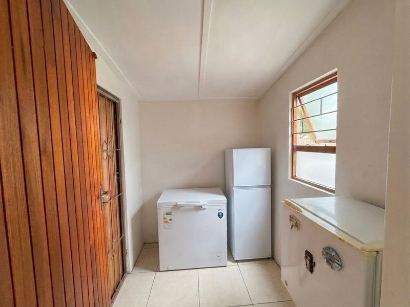 A functional scullery or utility area featuring tiled flooring, timber wall paneling, and a window with security bars.
