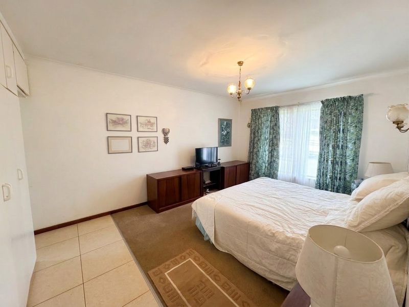 A spacious bedroom featuring built-in cupboards, a mix of tiled and carpeted flooring, and a classic ceiling rose fixture.