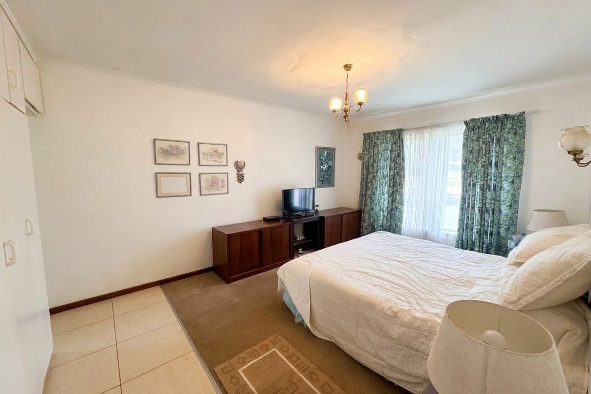 A spacious bedroom featuring built-in cupboards, a mix of tiled and carpeted flooring, and a classic ceiling rose fixture.