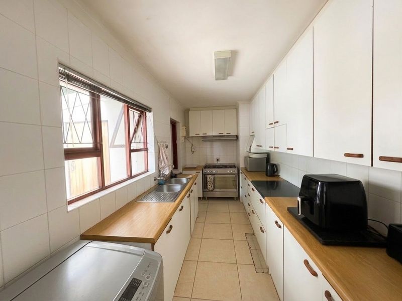 A functional galley-style kitchen featuring white cabinetry, wooden countertops, a gas stove, and tiled finishes throughout.
