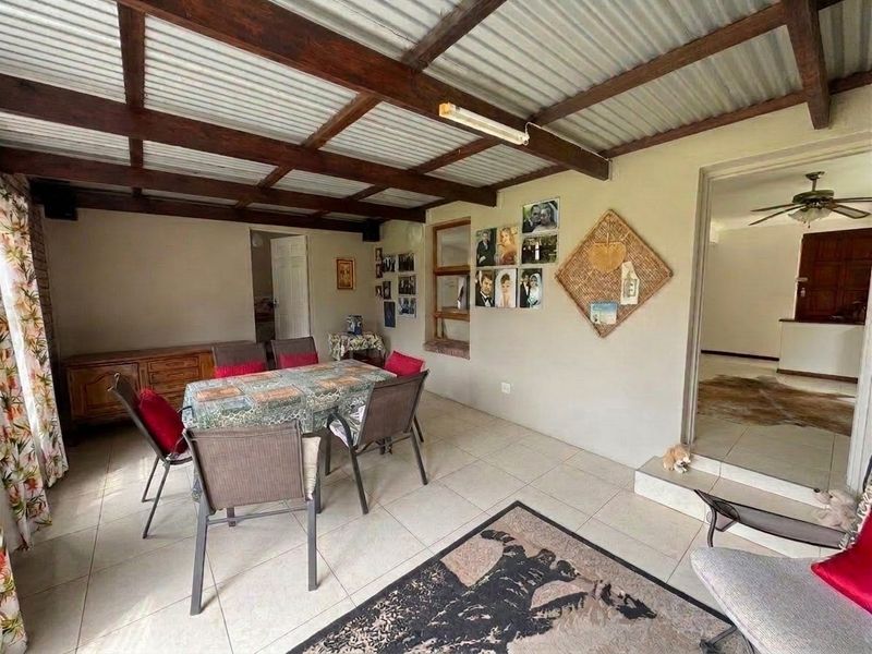 A covered patio area featuring exposed timber beams, corrugated metal roofing, and tiled flooring, providing a functional outdoor entertainment space.