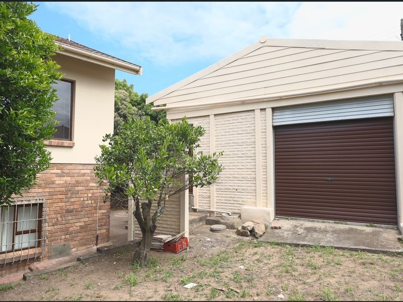 Rear view of the property showing a detached garage with a roller door, brick and cladding exterior, and an unpaved garden area.