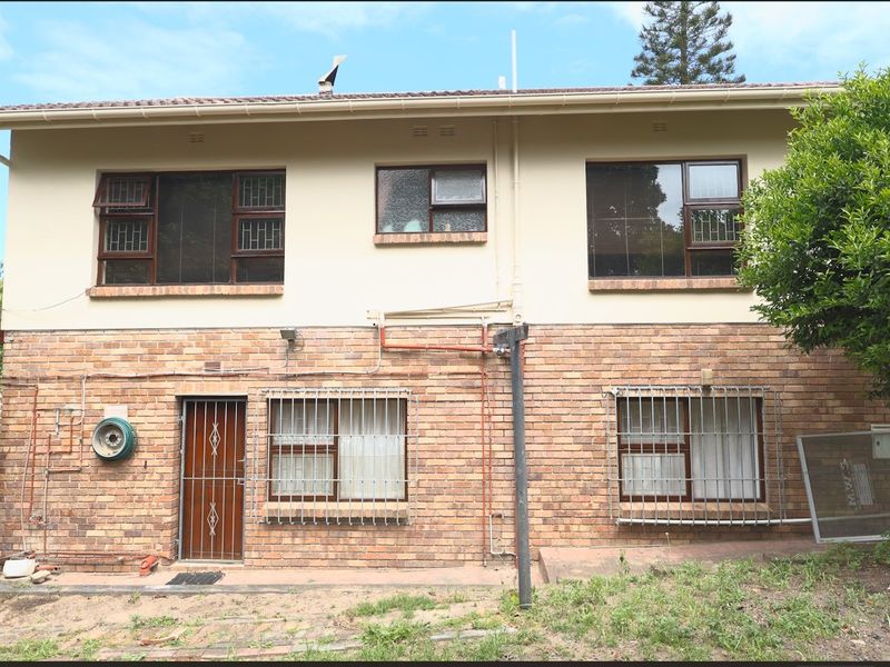 Rear elevation of a two-story brick and plaster house featuring security bars on windows and ground-level access.