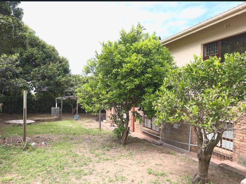 A view of the rear exterior of the house featuring a brick facade, security window bars, and a large garden area with mature trees.