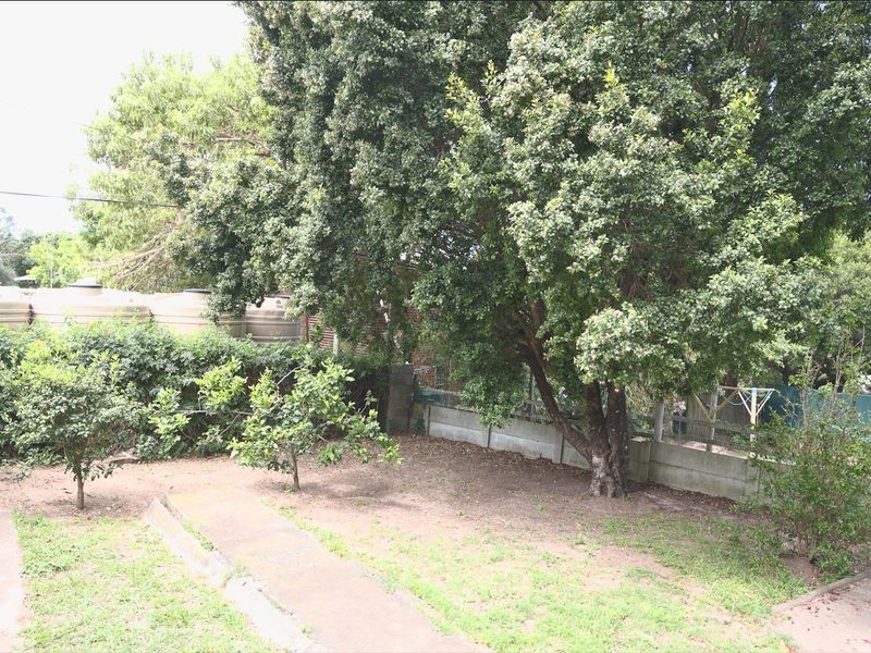 A spacious backyard area featuring mature trees, a concrete boundary wall, and installed water storage tanks.