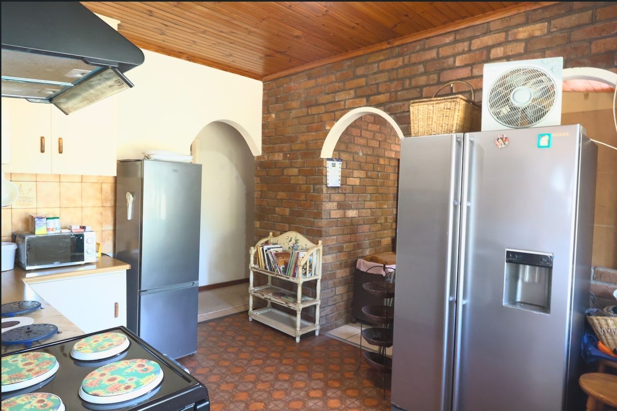 A kitchen featuring exposed brick walls, timber ceiling, and arched doorways, offering a rustic aesthetic with functional built-in cabinetry and an extractor fan.