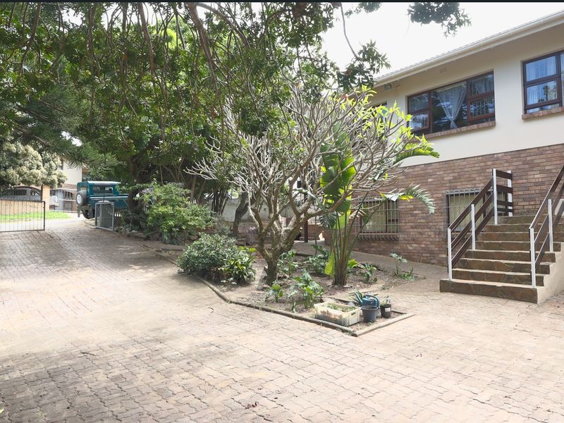 Front exterior view featuring a paved driveway, landscaped garden bed, and an external staircase leading to the upper level of the brick-faced house.