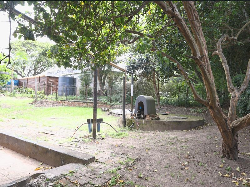 A spacious garden area featuring a borehole pump, water storage tank, brick paving, and established trees, offering potential for landscaping and outdoor development.