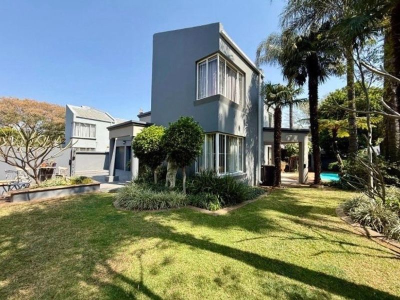 A well-maintained rear exterior view of a modern two-story house featuring corner windows, a covered patio area, and a landscaped garden.