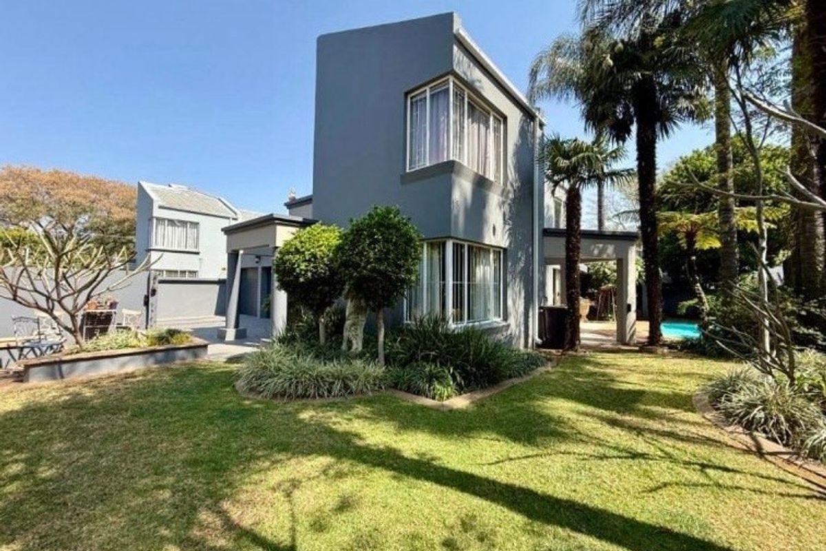 A well-maintained rear exterior view of a modern two-story house featuring corner windows, a covered patio area, and a landscaped garden.