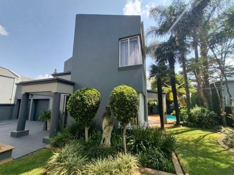 A modern two-story home exterior featuring a paved driveway, covered entrance, landscaped garden, and a glimpse of a swimming pool in the rear.