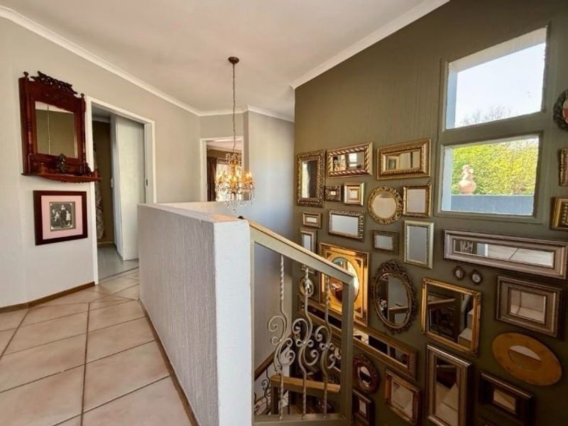 A bright upper-level hallway featuring tiled flooring, a decorative wrought iron balustrade, and a feature wall with natural light from adjacent windows.