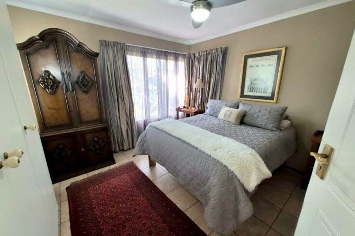 A cozy bedroom featuring tiled flooring, a ceiling fan, and large windows with curtain rails, offering a comfortable and functional living space.