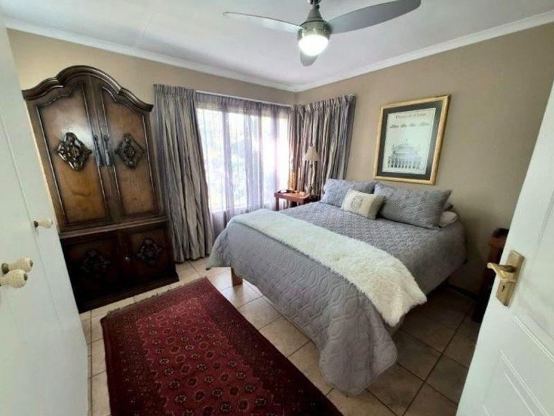 A cozy bedroom featuring tiled flooring, a ceiling fan, and large windows with curtain rails, offering a comfortable and functional living space.