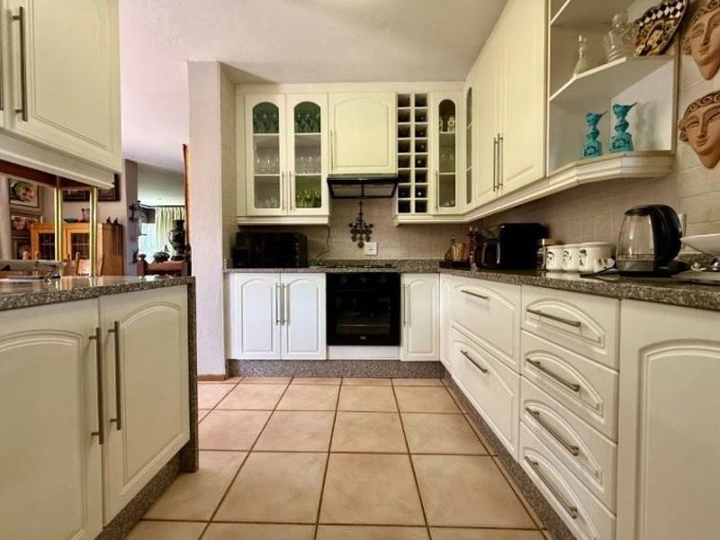 A functional kitchen featuring white cabinetry, granite countertops, built-in oven, extractor fan, and ceramic tile flooring with integrated wine storage.