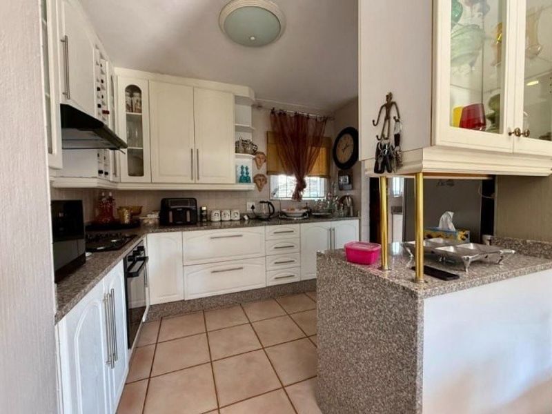 A functional kitchen featuring white cabinetry, granite countertops, and tiled flooring, offering a practical layout with integrated cooking appliances.