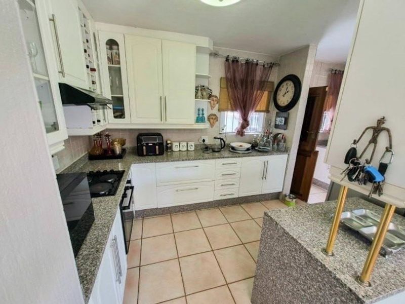 A functional kitchen featuring granite countertops, white cabinetry, and tiled flooring, offering a practical layout with integrated cooking appliances.