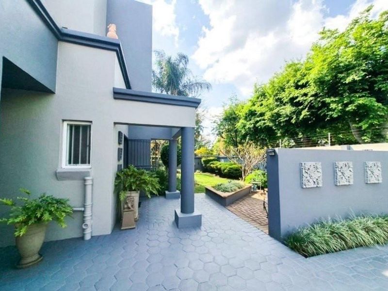 A well-maintained covered patio area featuring paved flooring, a low retaining wall, and landscaped garden surroundings.