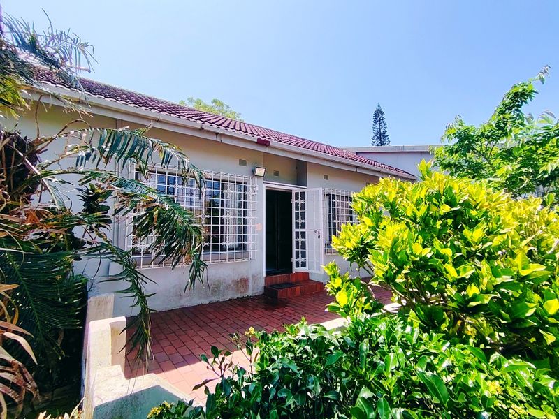 Rear exterior view of the townhouse featuring a brick patio, security bars on windows, and a tiled roof.
