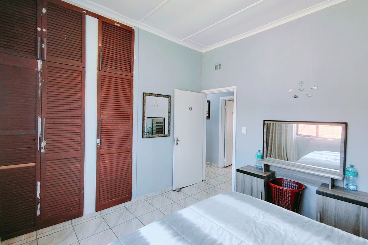 A bedroom featuring built-in wooden louvered cupboards and tiled flooring, offering a functional space with potential for cosmetic updates.
