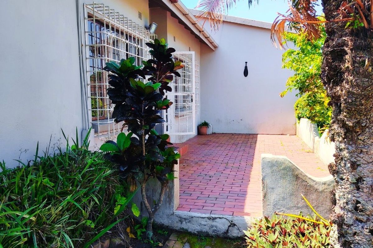 A rear exterior view of the townhouse featuring a brick-paved patio area, security bars on windows, and a concrete retaining wall.