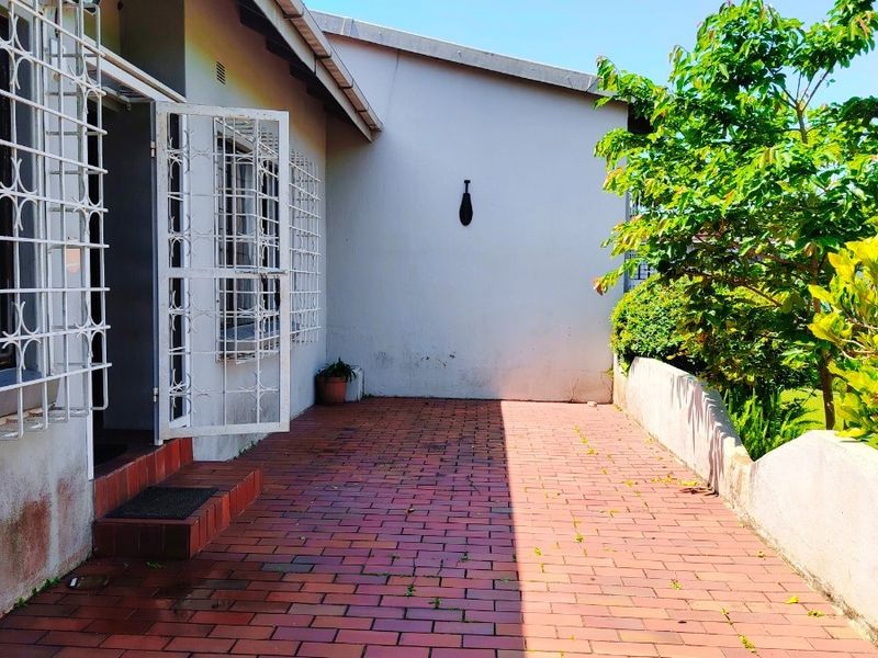 A paved outdoor patio area featuring security gates and bars, bordered by a low retaining wall and established garden greenery.