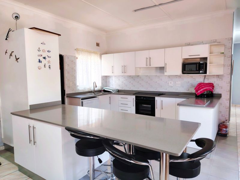 Modern kitchen featuring white cabinetry, stone countertops, a breakfast bar, and built-in appliances including an oven and hob.