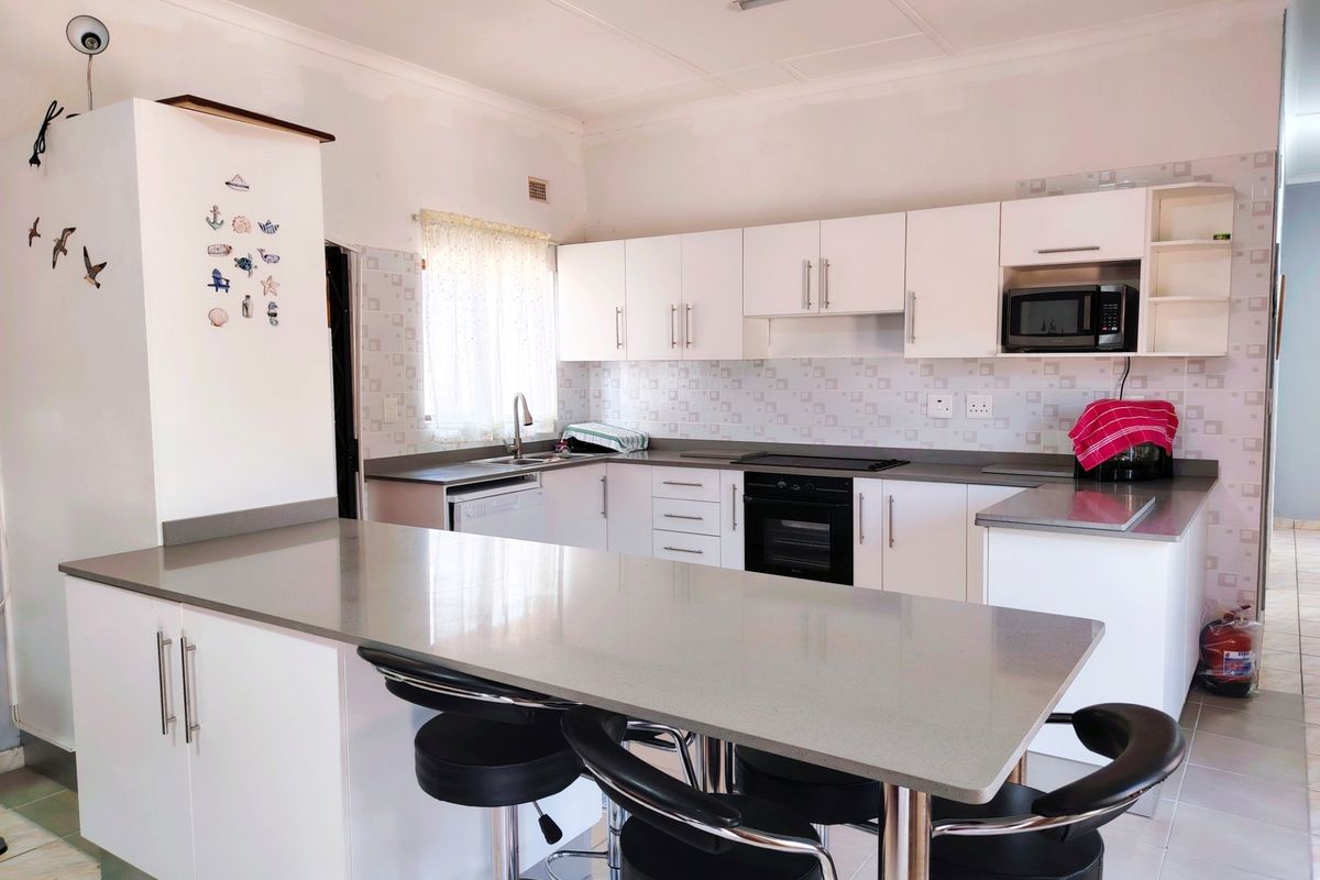 Modern kitchen featuring white cabinetry, stone countertops, a breakfast bar, and built-in appliances including an oven and hob.