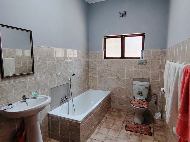 A functional bathroom featuring a pedestal basin, built-in bathtub, and toilet with neutral tiled finishes and wall-mounted mirror.
