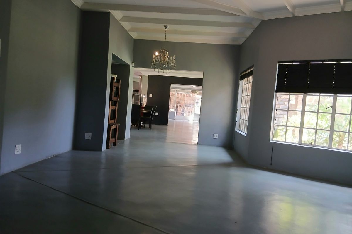 Spacious living area featuring polished concrete floors, exposed beam ceilings, and large grid-pattern windows, offering a bright and open atmosphere.