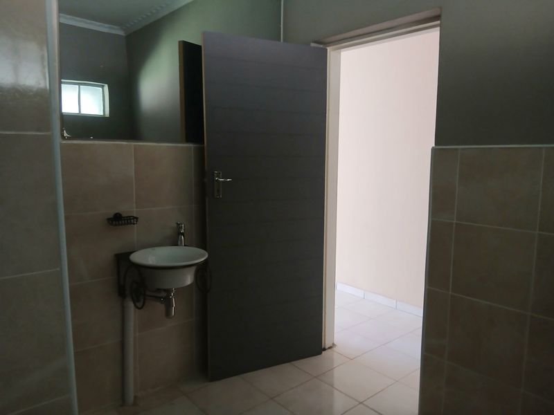 A functional bathroom featuring a wall-mounted basin, tiled surfaces, and a mirror, providing a clean and simple layout.