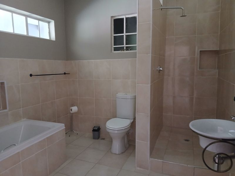 A functional bathroom featuring a built-in bathtub, a separate walk-in shower with a niche, a toilet, and a pedestal sink with neutral tiling.