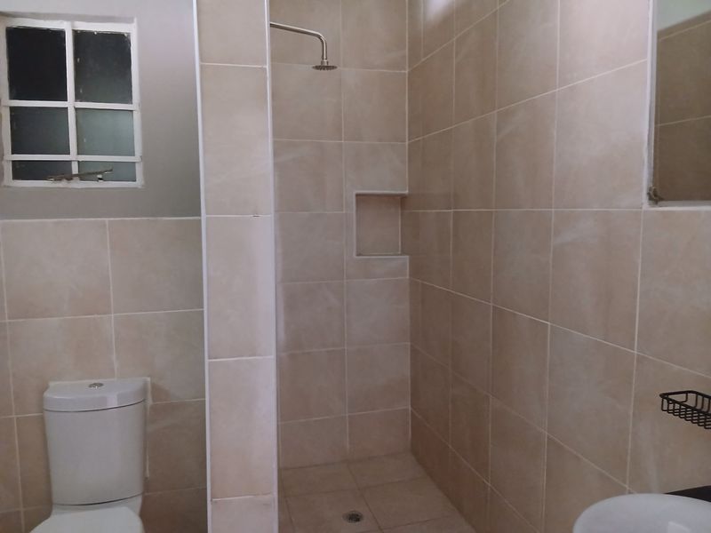 A functional bathroom featuring a walk-in shower with a built-in niche, neutral wall tiling, a standard toilet, and a basin.