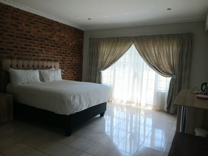 Spacious bedroom featuring an exposed brick accent wall, tiled flooring, and large sliding glass doors that provide ample natural light.