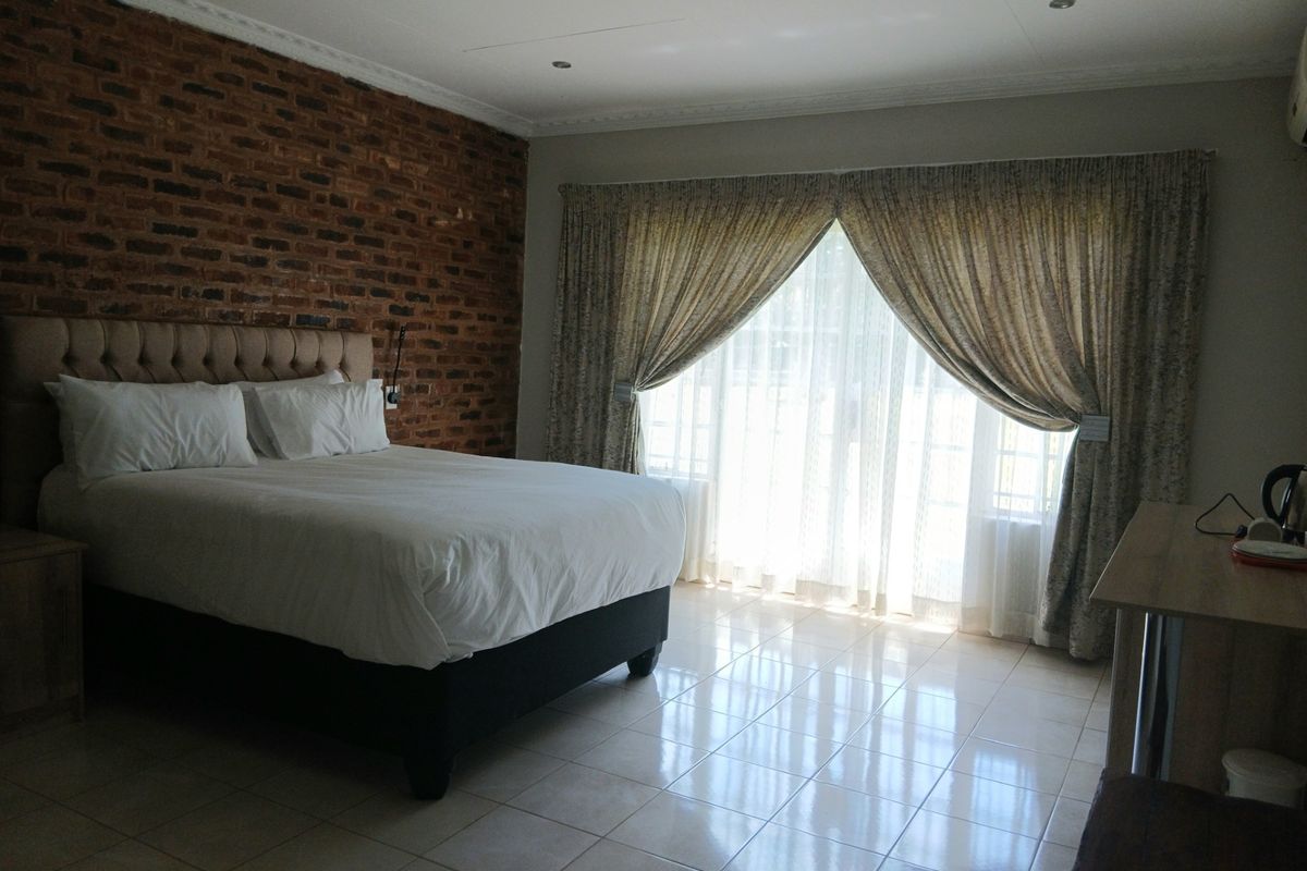Spacious bedroom featuring an exposed brick accent wall, tiled flooring, and large sliding glass doors that provide ample natural light.