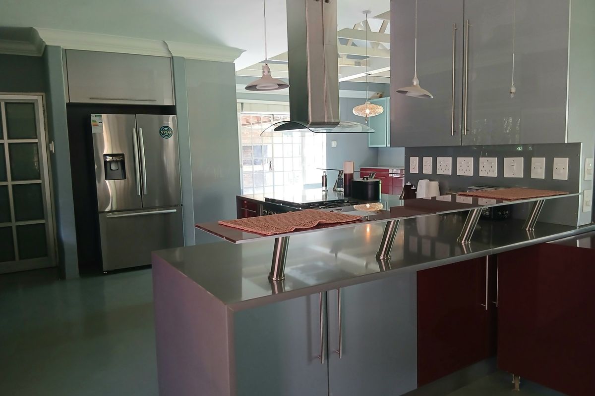 Modern kitchen featuring sleek grey and burgundy cabinetry, a central island with breakfast bar, stainless steel extractor fan, and integrated appliance space.