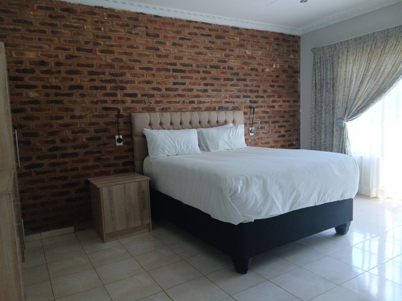 Spacious bedroom featuring a prominent exposed brick feature wall, neutral tiled flooring, and elegant ceiling cornicing.