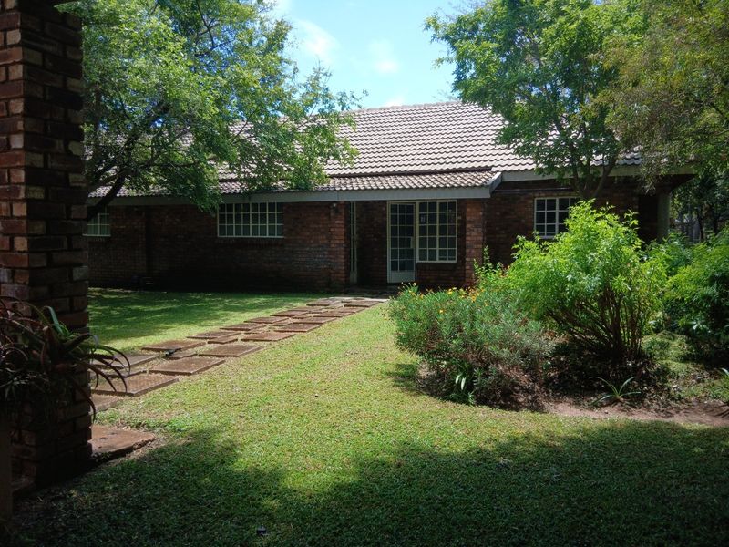 A view of the rear exterior of the house featuring a brick facade, tiled roof, and a paved walkway leading through the garden.