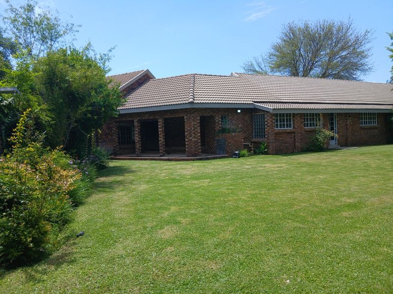 A view of the rear elevation of the brick house, featuring a covered patio area and a well-maintained lawn.