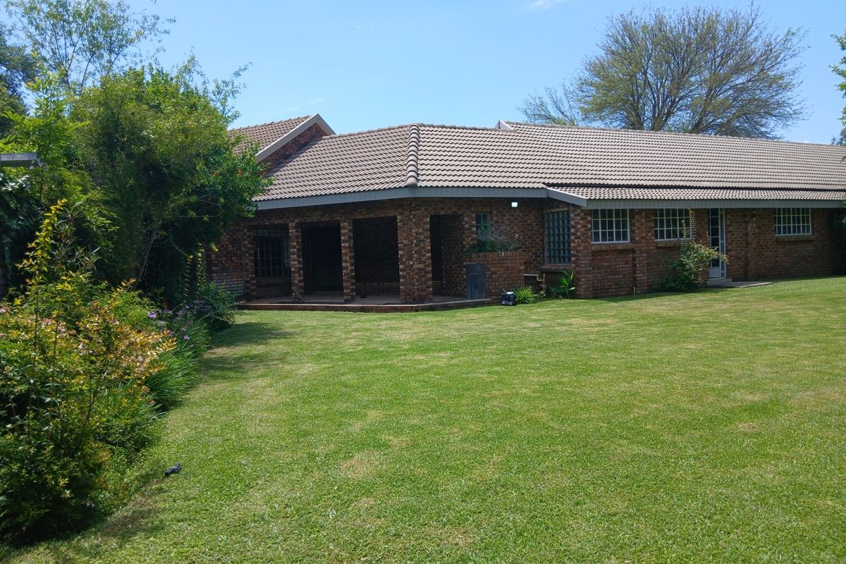 A view of the rear elevation of the brick house, featuring a covered patio area and a well-maintained lawn.