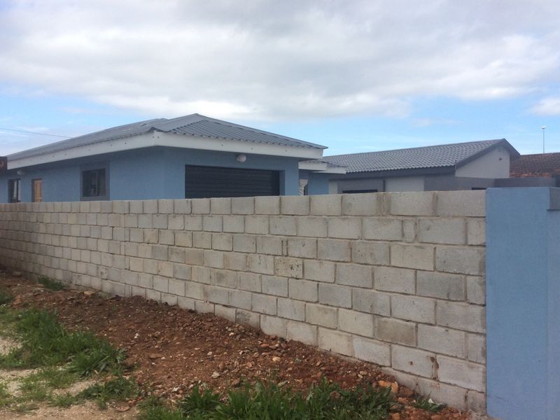 Exterior view of a residential property featuring a blue painted facade, metal roofing, and an unfinished concrete block boundary wall.