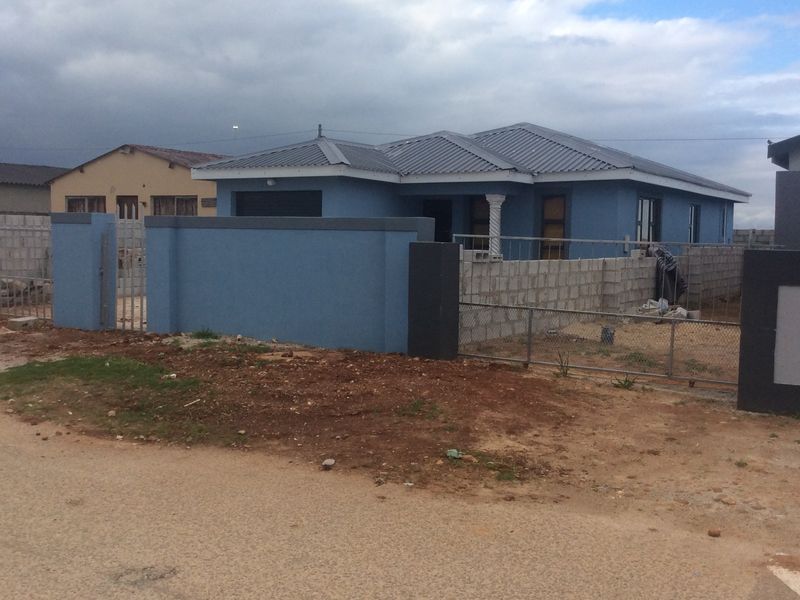 Front view of a blue-painted house featuring a corrugated metal roof, decorative column, and an ongoing perimeter wall construction project.
